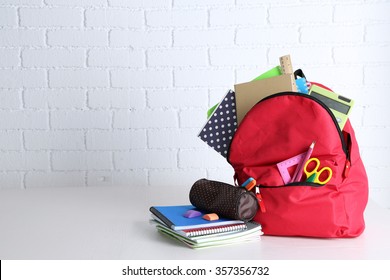 Backpack with school supplies on wooden table, on wall background - Shutterstock ID 357356732