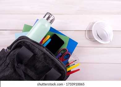 Backpack with school supplies, water bottle, cellphone and face mask on white Wooden background.