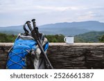 A backpack and trekking poles rest against a rustic log, alongside a mug, overlooking a scenic mountain view. The setup captures the essence of a peaceful hiking adventure in nature.