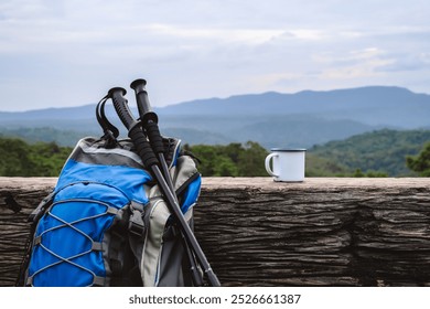 A backpack and trekking poles rest against a rustic log, alongside a mug, overlooking a scenic mountain view. The setup captures the essence of a peaceful hiking adventure in nature. - Powered by Shutterstock