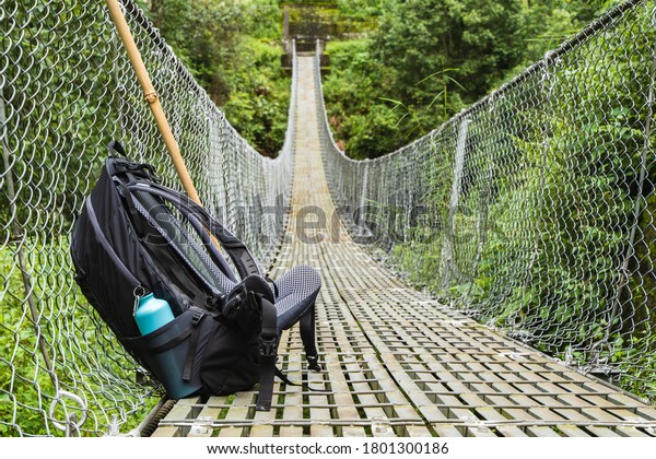 Backpack\
with water bottle and bamboo stick on pedestrian suspension bridge.\
Mountain hiking, trekking concept. Stock\
photo