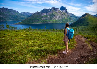 backpacker girl hiking hesten trailhead overlooking the town of fjordgard and mighty mountains in norway, senja island hiking, famous segla mountain