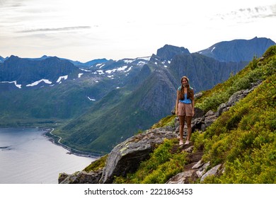 backpacker girl hiking on hesten overlooking Norway's famous segla mountain, senja island; hesten trail head, Norway's famous fjords with mighty mountains above the sea