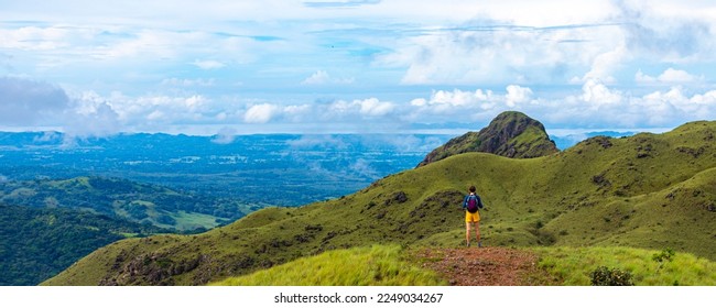 A backpacker girl stands on top of Costa Rica's cerro pelado mountains during a sunny day; hiking through mighty mountains covered with green succulent grass; mountains in the tropics amid rainforests - Shutterstock ID 2249034267