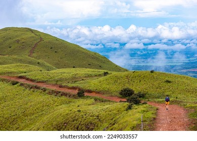 backpacker girl walks along a ridge among Costa Rica's cerro pelado mountains during a sunny day; hiking through mighty mountains covered with green, luscious grass; mountains in the tropics amid rain