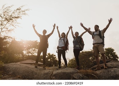 Backpacker Group Of Four Asian Men And Women Standing At The Top Of The Mountain, Raising Your Hands In Joy And Success.