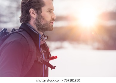 Backpacker Man Detail Wearing Anorak Jacket. Exploring Snowy Land Walking And Skiing With Alpine Ski. Europe Alps. Winter Sunny Day, Snow, Wide Shot, Warm Sun Flare.travelling, Side View