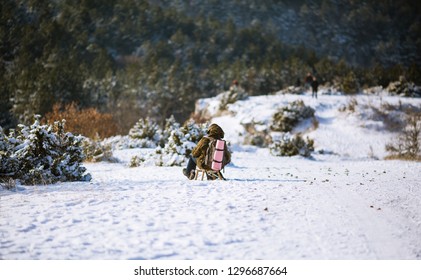 Backpacker man sledging down a snow covered hill. Winter in mountains.
