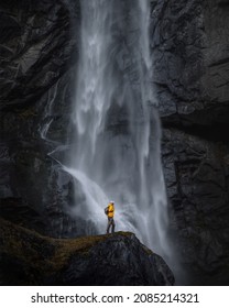 
				Backpacker man in yellow jacket explores waterfall in Switzerland