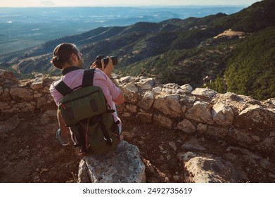 A backpacker and photographer captures a scenic mountain landscape from a rocky viewpoint. The image evokes feelings of adventure, exploration, and nature. - Powered by Shutterstock