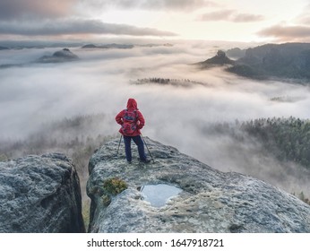 Backpacker stay on wet rock. Misty daybreak in rocky mountains. Hiker with backpack stand on rocky view point above valley. Vivid and strong vignetting effect - Powered by Shutterstock