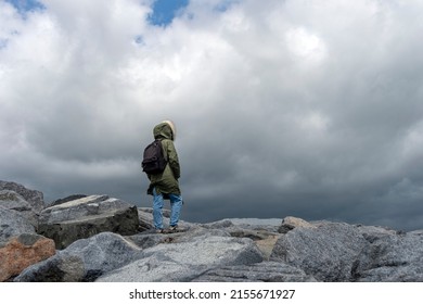 Backpacker At Top Of A Rocky Mountain Pass With A Stormy Sky And High Winds.