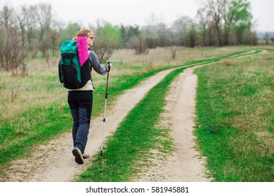 Backpacker woman with trekking pole in hand , walking with a backpack. ahead her rural road