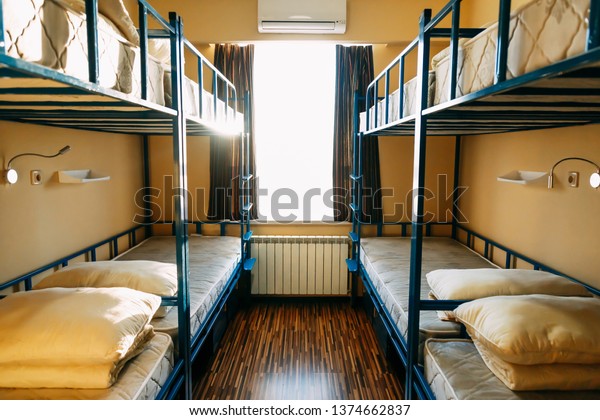Backpackers stay in hotel with modern\
double-decker beds inside the dorm room for twelve people. Window\
in bedroom of a youth\
hostel