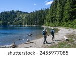 Backpackers walking on the shore of Summit Lake. Dog playing in the lake. Mount Rainier National Park. Washington State.
