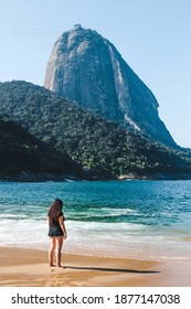 Backpacking girl views Sugarloaf Mountain or Pão de Açúcar from the clean sands and turquoise water of Praia Vermelha in Rio de Janeiro, Brazil