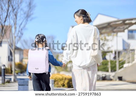 The backs of a parent and child walking hand in hand through a residential area.
