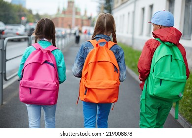 Backs of schoolkids with colorful rucksacks moving in the street