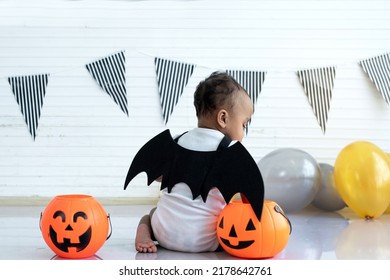 Backside of African baby child girl wearing black winged vampire with orange candy bucket Jack O lantern, Haloween costume, Happy Halloween