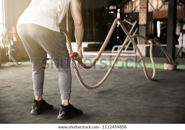 Backside of Asian\
man exercise doing rope workout working out arms and cardio in\
fitness. exercise\
concept.