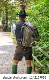 backside of bavarian man with backpack walking on path