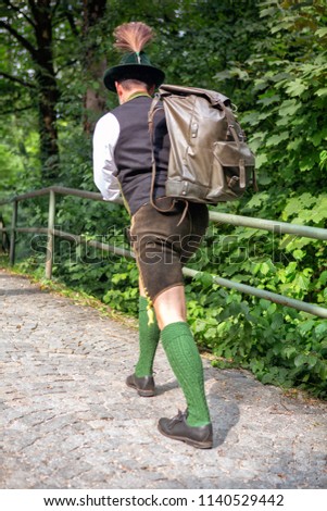 backside of bavarian man with backpack walking on path