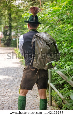 backside of bavarian man with backpack walking on path