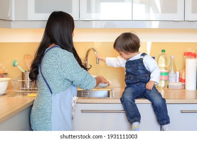 Backside Of Happy Young Mother Cleaning Dishes With Her Kid At Kitchen Home. Asian Woman Teaching Her Child With Housework.