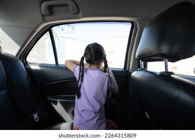 Backside of Little Asian 5 years old girl, is looking to the outside through car window mirror in the afternoon time.