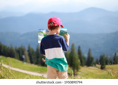 Backside of toddler boy standing on top of the mountain and looking a map in the summer sunny day. Happy kid on vacation with beautiful alpine mountain on background. Bavaria, Germany.