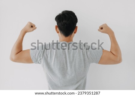 Backside view of Asian man back wear grey t-shirt raising arms, showing muscles biceps power, healthy body builder isolated over white background wall.