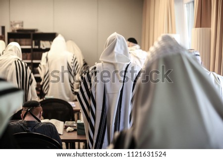 Backside view of congregants in a Jewish synagogue wrapped in prayer shawls during prayer