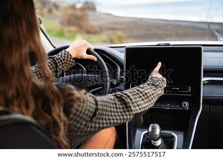 Backside view of an unrecognizable woman using a GPS navigation system while driving her car. Female driver touching modern car dashboard. Screen multimedia system in automobile. Inside auto salon.