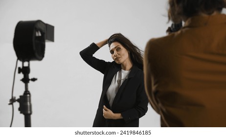 Backstage of model and professional team in the studio. Close up of attractive model in suit posing, photographer taking pics, positive expression.