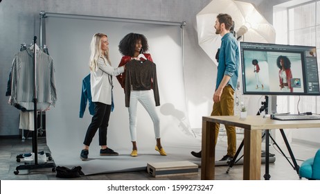 Backstage Of The Photo Shoot: Stylist Chooses Outfit And Clothes For A Beautiful Black Model Girl, Photographer Ready To Shoot. Professional Fashion Magazine Studio Photoshoot