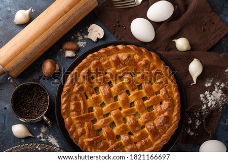 The backstage of preparing homemade pie witch mushrooms. The rolling pin. some eggs. fork. black pepper. garlic isolated on brown napkin. Dark background.