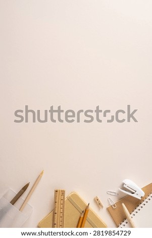Backtoschool stationery flatlay featuring notebook, pencil, ruler, stapler and paperclip arranged on a beige desk to evoke study, organization and creative planning