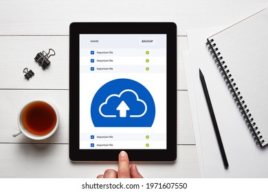 Backup cloud storage concept on tablet screen with office objects on white wooden table. Flat lay