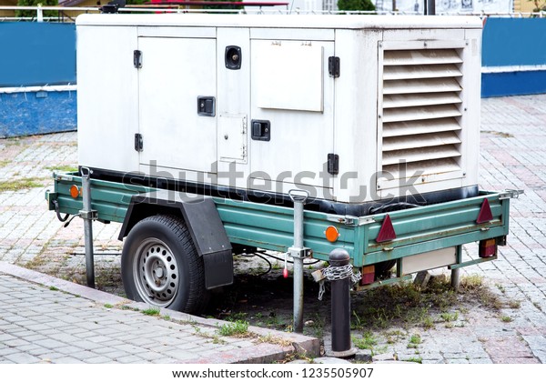 backup power\
generator mounted on a car trailer on wheels standing on a city\
street paved with paving\
slabs.
