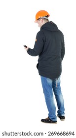 Backview Of An Engineer In Construction Helmet Stands And Using A Mobile Phone. Standing Young Guy. Rear View People Collection.  Backside View Of Person.  Isolated Over White Background.