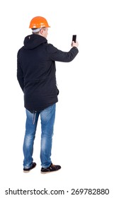 Backview Of An Engineer In Construction Helmet Stands And Using A Mobile Phone. Standing Young Guy. Rear View People Collection.  Backside View Of Person.  Isolated Over White Background.