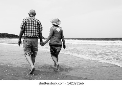 Backview Of Senior Couple Walking On Sandy Beach