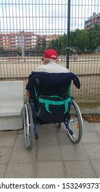 Backwards View Of An Lonely Old Man On A Wheel Chair Looking To A Park Behind A Fence - Image