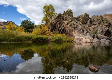 Backwater pool on Cache la Poudre canyon in Fort Collins, CO.  Huge rock bluff, blue sky and trees along white clouds.  Pond foreground.  Scenic area with blue sky, reflective water and rock bluff .