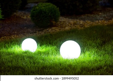 Backyard 2 Light Garden With Lantern Electric Lamp With Sphere Diffuser In Green Grass With Thuja Bushes And Stone Mulching In Park With Landscaping, Closeup Night Scene Nobody.