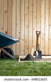 A Backyard, DIY, Home Garden Concreting Project With Wheelbarrow, Shovel, Wooden Fence, Wet Cement And Form Work.