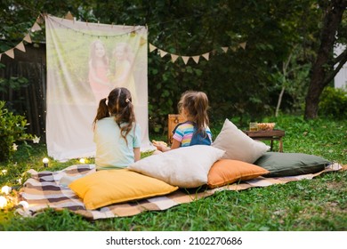 Backyard Family outdoor movie night with kids. Sisters spending time together and watching cimema at backyard. DIY Screen with film. Summer outdoor weekend activities with children. Open air cinema. - Shutterstock ID 2102270686