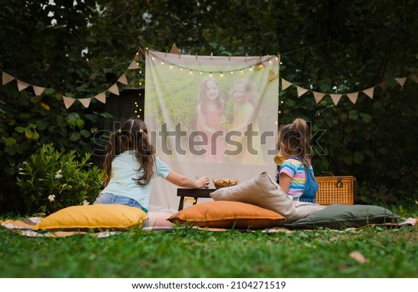 Backyard Family outdoor movie night with kids.\
Sisters spending time together and watching cimema at backyard. DIY\
Screen with film. Summer outdoor weekend activities with children.\
Open air cinema.