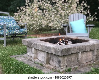 Backyard Fire Pit With Adirondack Chairs And Blue Pillow In Green Summer Grass 