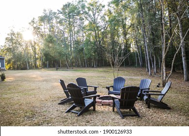 A Backyard Fire Pit In A Spacious Yard Of A Large Home With Several Adirondack Chairs